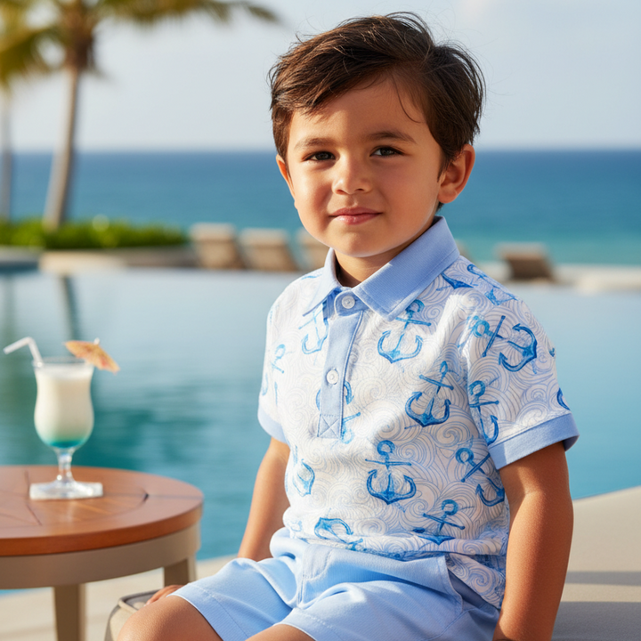 Child in a polo shirt with anchor pattern sitting by a pool with palm trees and ocean in the background